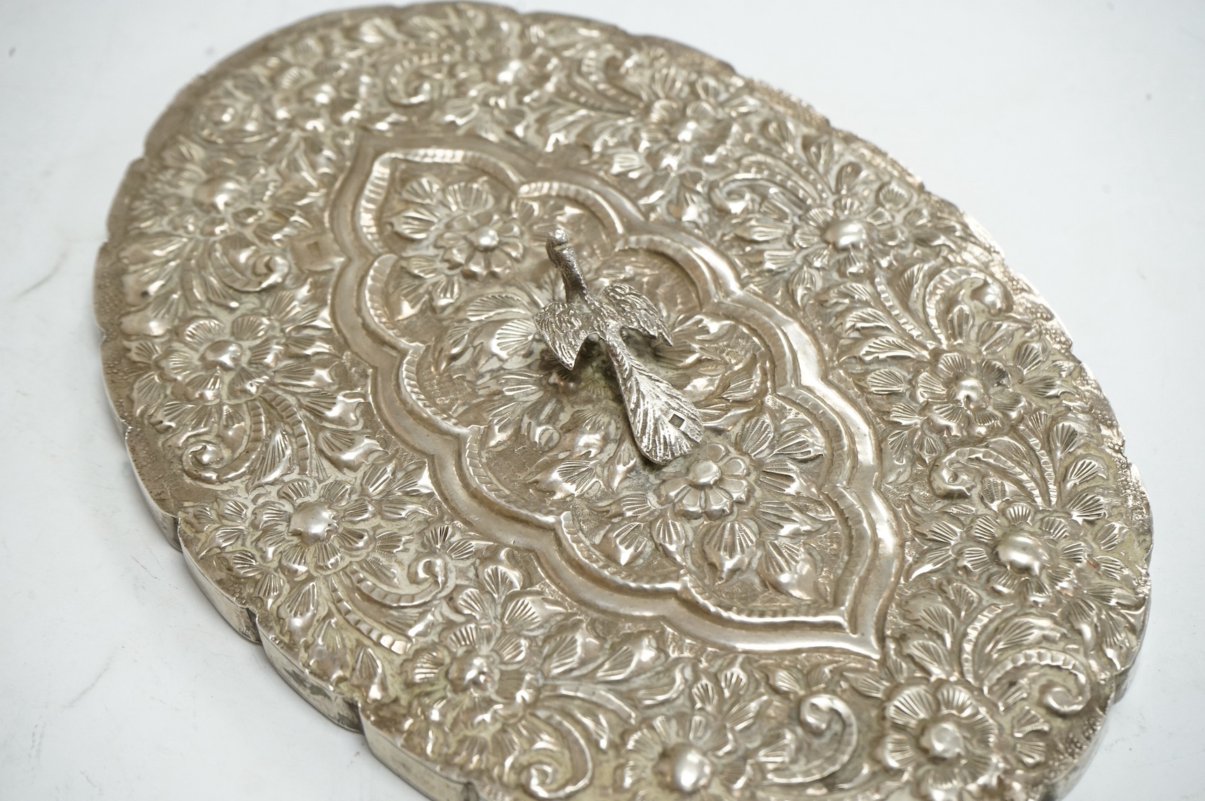 An Egyptian embossed 900 standard? white metal oval hand mirror, with bird handle and decorated with foliage, plate a.f., 20.5cm. Condition - poor to fair